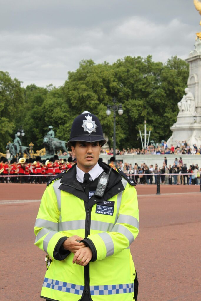 A British police officer on duty near Buckingham Palace with a marching band in the background.